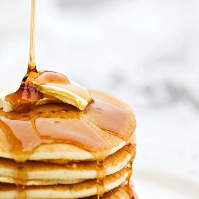 A stack of pancakes with syrup being poured on them.